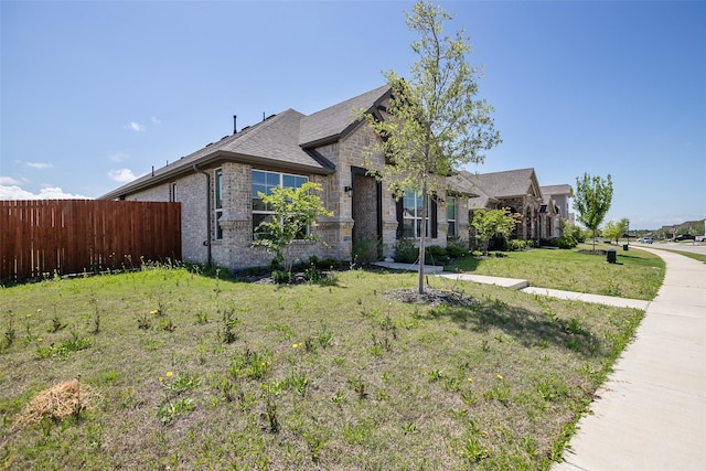 view of front of house with brick siding, fence, a shingled roof, and a front yard