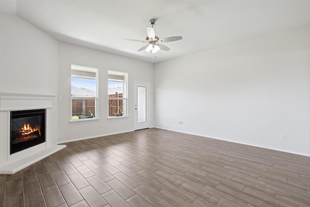 unfurnished living room featuring dark wood-style flooring, ceiling fan, a glass covered fireplace, and baseboards
