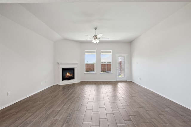 unfurnished living room featuring a glass covered fireplace, baseboards, a ceiling fan, and dark wood-style flooring