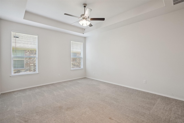 carpeted spare room with a ceiling fan, a tray ceiling, visible vents, and baseboards