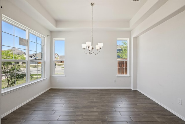 unfurnished dining area featuring a notable chandelier, a healthy amount of sunlight, a raised ceiling, and dark wood-type flooring