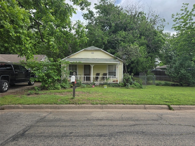 bungalow featuring covered porch, fence, and a front yard