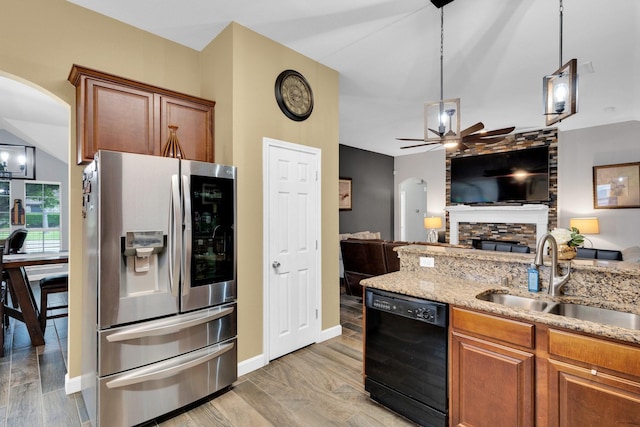 kitchen featuring a sink, stainless steel fridge with ice dispenser, dishwasher, arched walkways, and brown cabinetry