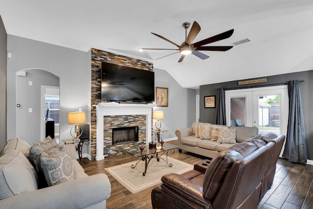 living area featuring ceiling fan, arched walkways, a stone fireplace, vaulted ceiling, and visible vents