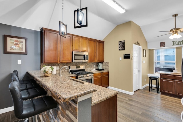 kitchen with baseboards, ceiling fan, light wood-style flooring, appliances with stainless steel finishes, and vaulted ceiling