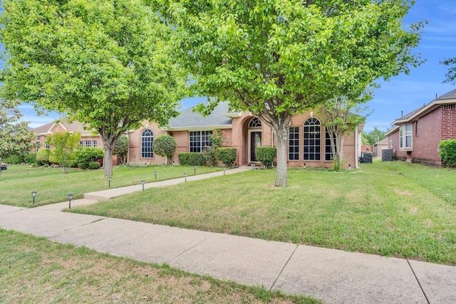 view of property hidden behind natural elements featuring brick siding, roof with shingles, and a front lawn