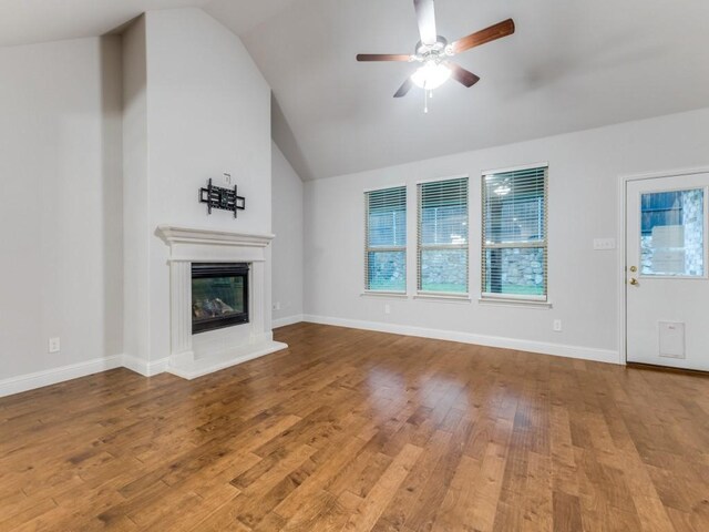 unfurnished living room featuring a glass covered fireplace, wood finished floors, lofted ceiling, baseboards, and a ceiling fan