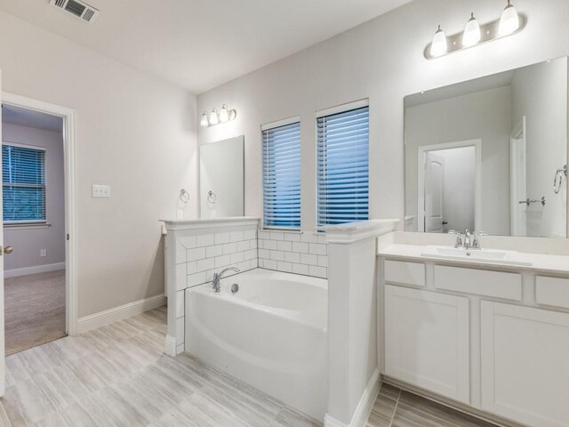 bathroom with baseboards, vanity, a bath, and visible vents