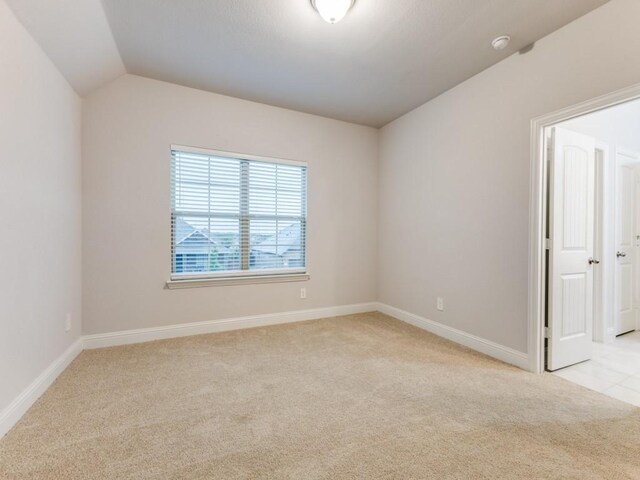 spare room featuring light colored carpet, baseboards, and lofted ceiling
