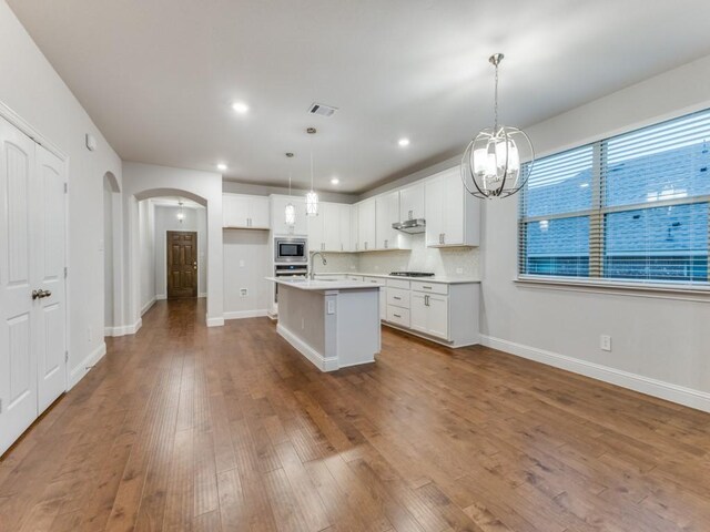 kitchen featuring arched walkways, a chandelier, dark wood finished floors, stainless steel appliances, and a center island with sink