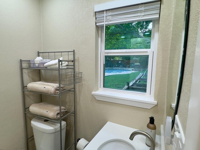 bathroom with toilet, a textured wall, and a sink