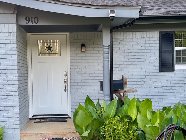 view of exterior entry featuring brick siding and roof with shingles