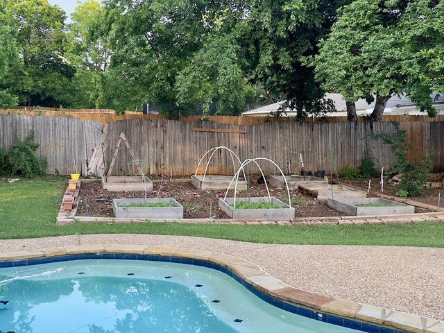 view of pool with fence, a lawn, and a garden