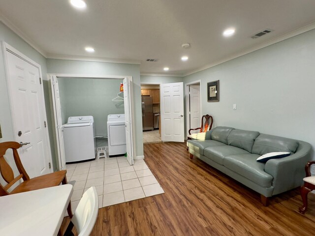 living room featuring crown molding, light wood-style floors, washer and clothes dryer, and visible vents
