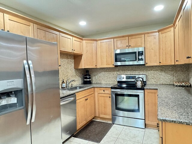 kitchen with light brown cabinets, a sink, stone counters, light tile patterned floors, and stainless steel appliances