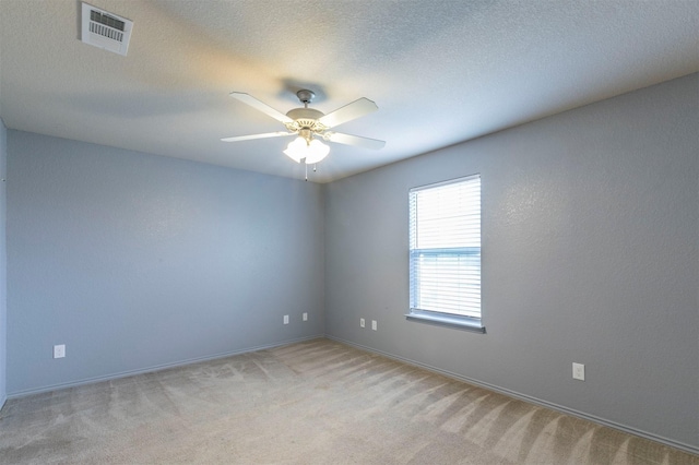 empty room featuring ceiling fan, a textured ceiling, light colored carpet, visible vents, and baseboards