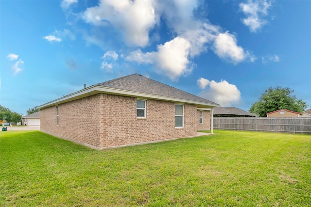 back of property with a yard, brick siding, fence, and roof with shingles