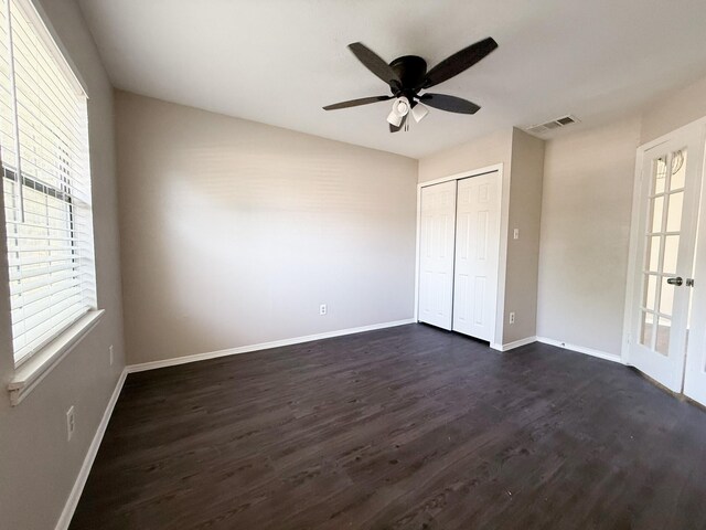 unfurnished bedroom with baseboards, visible vents, multiple windows, and dark wood-type flooring