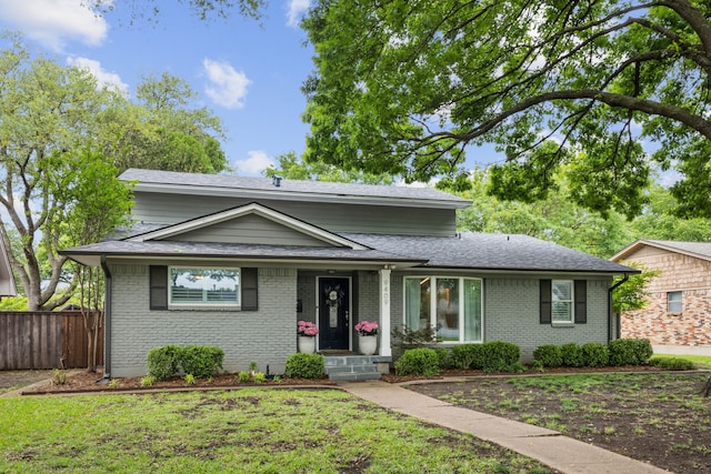 traditional-style home with brick siding, a shingled roof, a front lawn, and fence