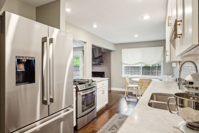 kitchen with a sink, baseboards, stainless steel appliances, white cabinetry, and dark wood-type flooring