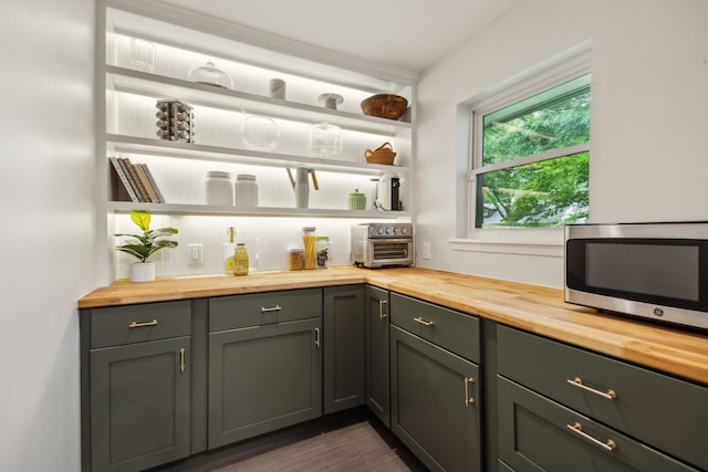 bar featuring dark wood-style flooring, stainless steel microwave, and a toaster