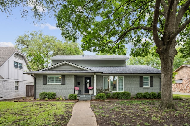 traditional home with covered porch, brick siding, and roof with shingles