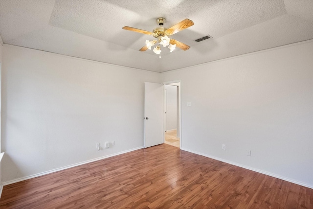 unfurnished room with a textured ceiling, a ceiling fan, wood finished floors, and visible vents
