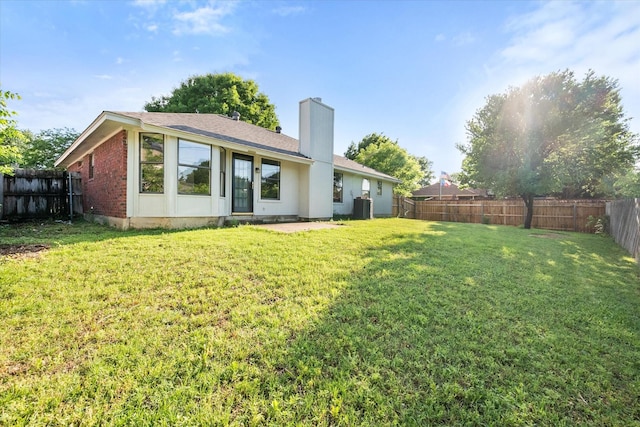 back of house featuring a lawn, a fenced backyard, central AC, and a chimney