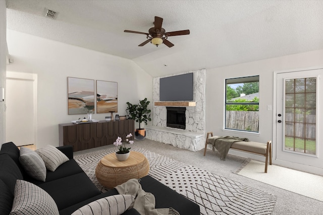 carpeted living room with ceiling fan, a fireplace, a textured ceiling, lofted ceiling, and visible vents