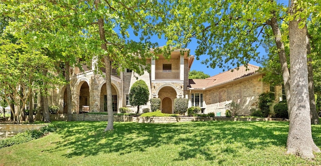 mediterranean / spanish-style home with a front yard, a tile roof, and stone siding