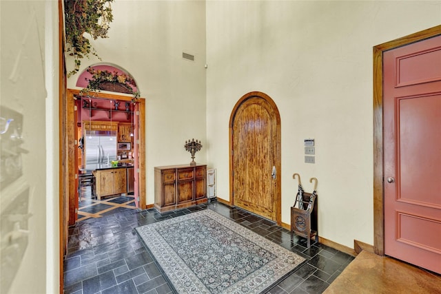 foyer with stone finish floor, a towering ceiling, visible vents, arched walkways, and baseboards