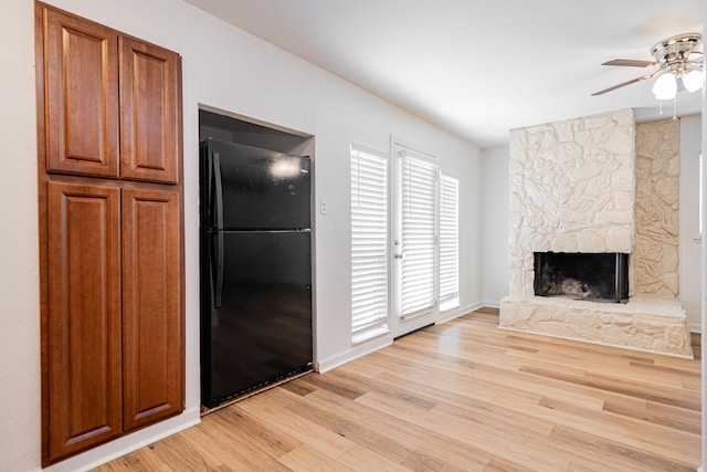 unfurnished living room featuring light wood-style floors, a ceiling fan, baseboards, and a stone fireplace
