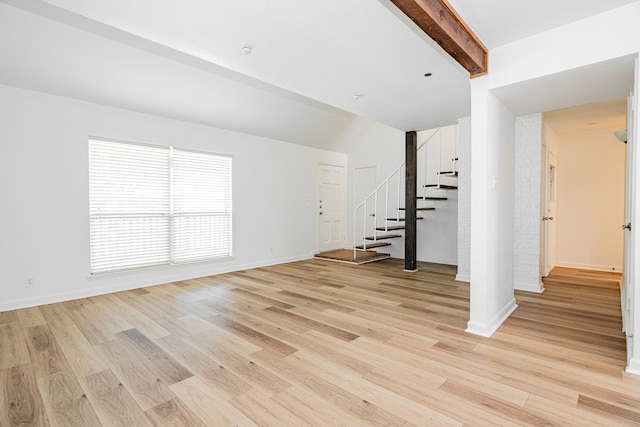 unfurnished living room with baseboards, light wood-style flooring, stairs, and lofted ceiling with beams