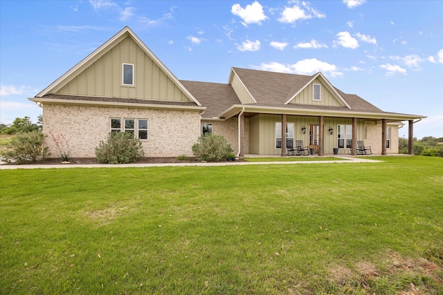 view of front facade with brick siding, a shingled roof, a front lawn, and board and batten siding