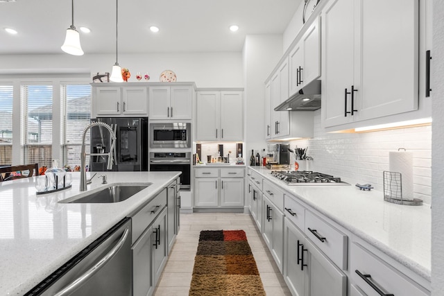 kitchen featuring hanging light fixtures, appliances with stainless steel finishes, a sink, tasteful backsplash, and under cabinet range hood