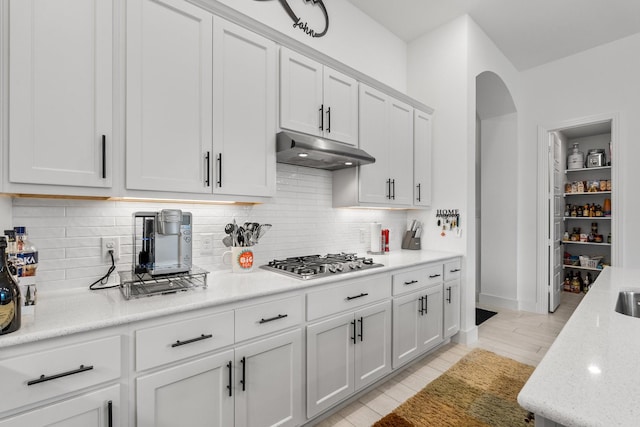 kitchen featuring under cabinet range hood, arched walkways, decorative backsplash, and stainless steel gas stovetop