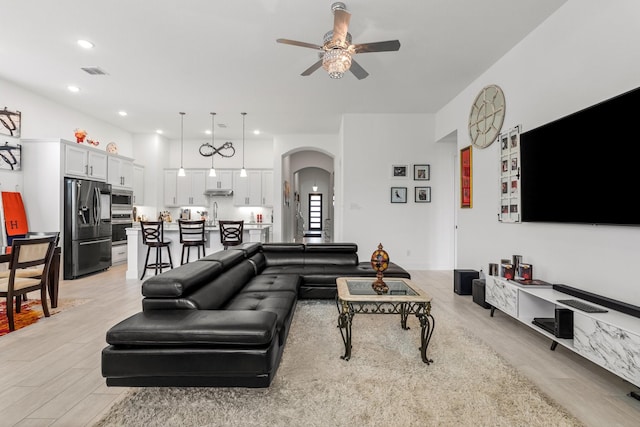 living room with ceiling fan, visible vents, arched walkways, light wood finished floors, and recessed lighting