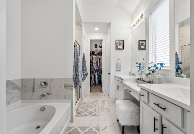 bathroom with vanity, marble finish floor, lofted ceiling, a bath, and a spacious closet