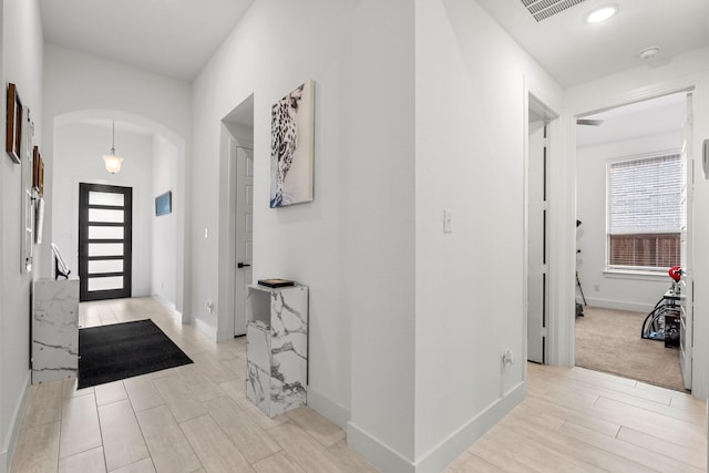 entrance foyer with arched walkways, baseboards, light wood-style flooring, and visible vents