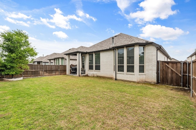 rear view of house featuring brick siding, a fenced backyard, a yard, and a shingled roof