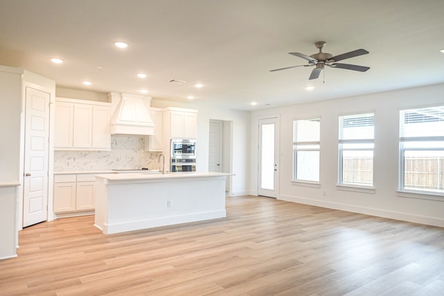 kitchen featuring decorative backsplash, custom range hood, light wood-style flooring, and white cabinets