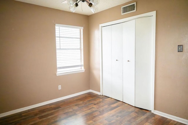 unfurnished bedroom with baseboards, visible vents, wood finished floors, and a closet