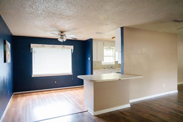 kitchen featuring visible vents, a peninsula, wood finished floors, light countertops, and white cabinets