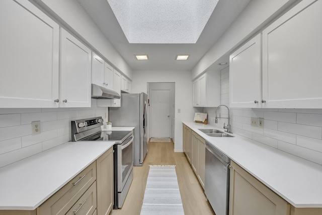 kitchen with appliances with stainless steel finishes, a sink, backsplash, light wood-type flooring, and under cabinet range hood