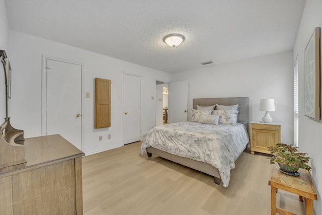 bedroom with light wood finished floors, a textured ceiling, and visible vents