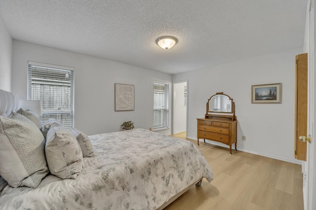 bedroom with light wood-style floors, baseboards, and a textured ceiling