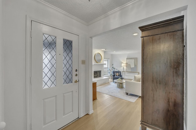 entrance foyer with a fireplace, ornamental molding, light wood-style flooring, and a textured ceiling