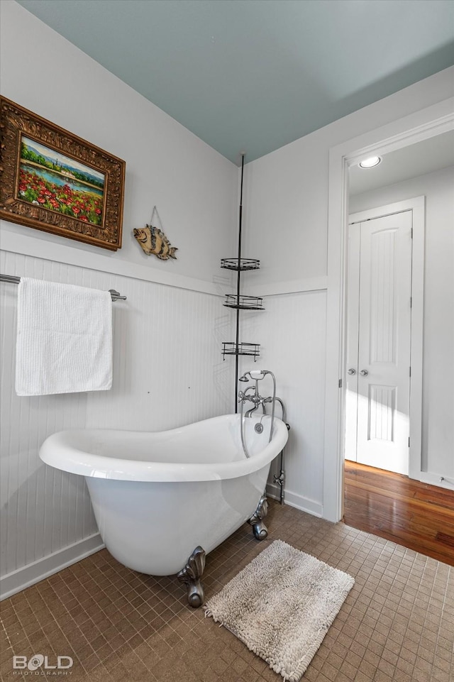 bathroom with a freestanding tub, a wainscoted wall, and tile patterned flooring