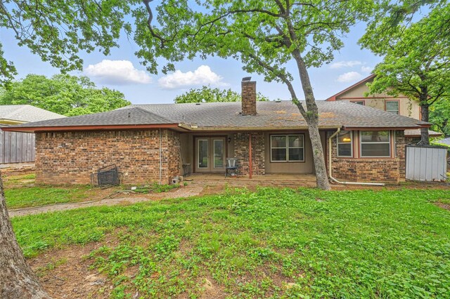 rear view of house with french doors, a chimney, a lawn, and brick siding