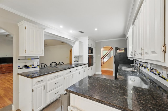 kitchen featuring white cabinets, a sink, arched walkways, backsplash, and black appliances